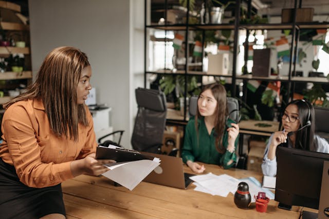 Three women meeting in a small business setting to discuss operational issues, reviewing paperwork and planning next steps.