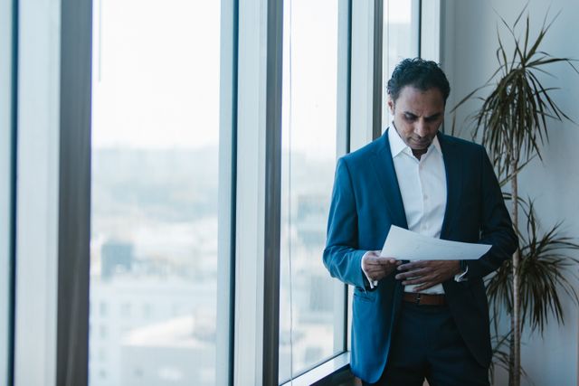 Business owner reviewing a document by an office window, weighing capital readiness for a new opportunity.