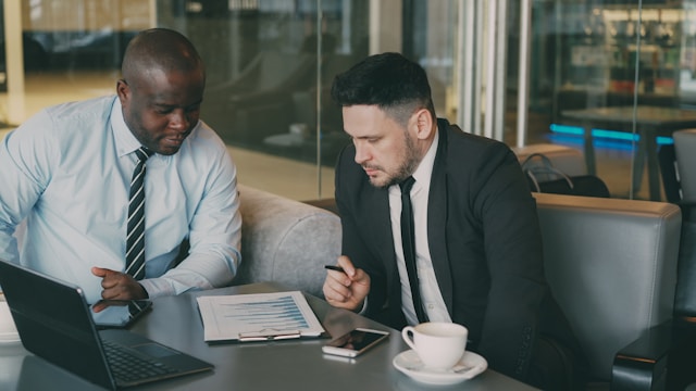 A small business owner and a lender review financial documents and a performance chart during a financing discussion at a table.
