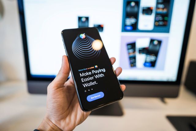 Smartphone showing a digital wallet payment screen in front of a blurred laptop, representing the payment fraud risk tied to growing digital wallet adoption